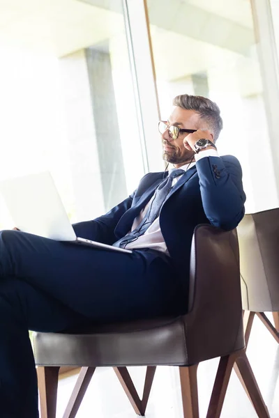 Hombre de negocios guapo en traje y gafas con auriculares usando el ordenador portátil - foto de stock