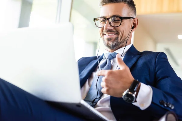 Hombre de negocios guapo y sonriente en traje y gafas usando el ordenador portátil - foto de stock