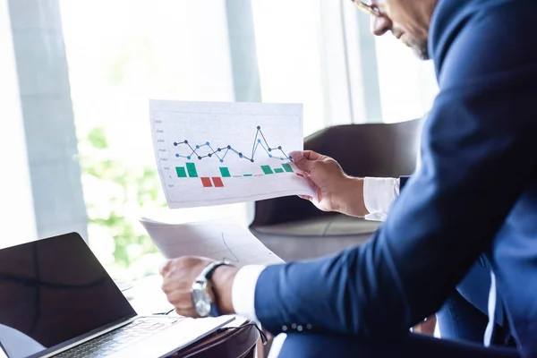 Cropped view of man in formal wear looking at papers with charts and graphs — Stock Photo
