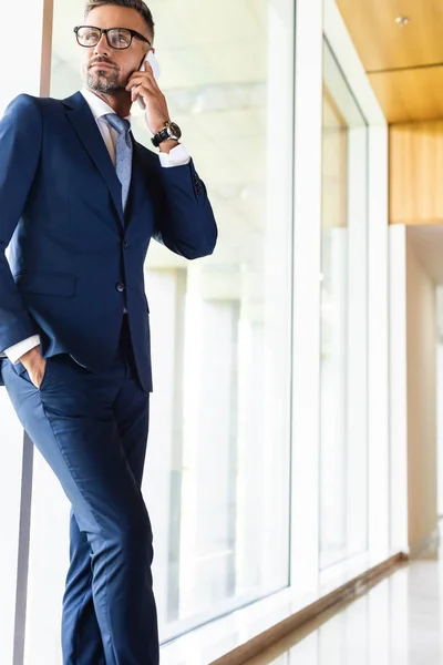 Hombre de negocios guapo en traje y gafas hablando en smartphone - foto de stock