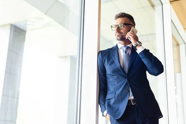 Handsome businessman in formal wear and glasses talking on smartphone — Stock Photo