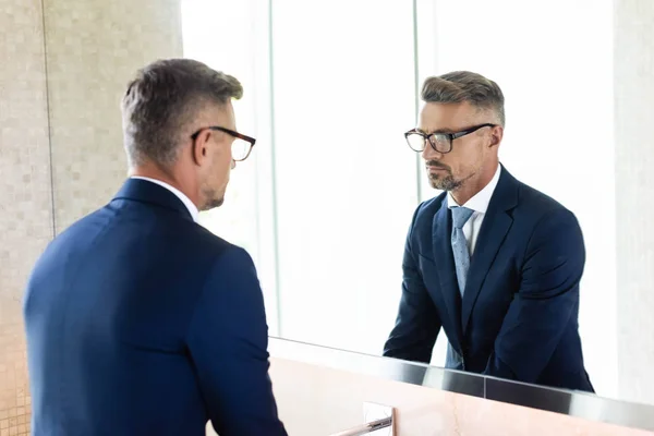 Schöner Geschäftsmann in formeller Kleidung und Brille, der in den Spiegel schaut — Stockfoto