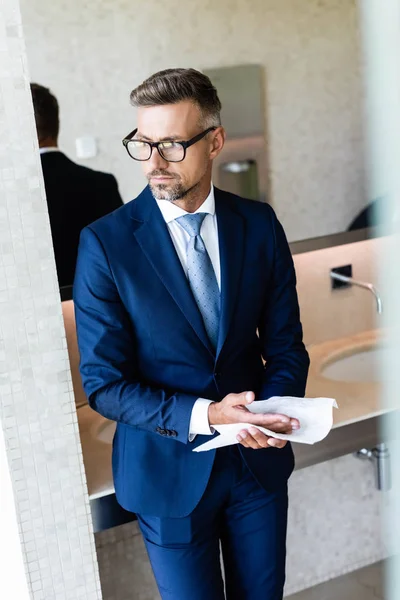 Guapo hombre de negocios en ropa formal y gafas limpiándose las manos - foto de stock