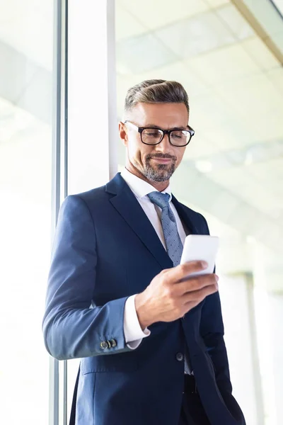 Hombre de negocios guapo en ropa formal y gafas usando teléfono inteligente - foto de stock