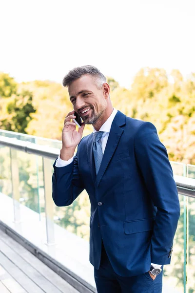 Handsome and smiling businessman in formal wear talking on smartphone — Stock Photo