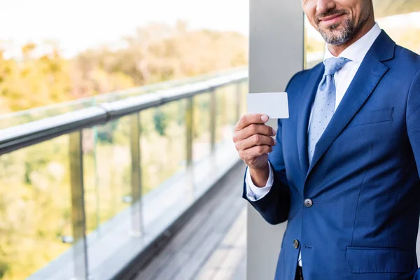 Visão recortada de homem de negócios sorridente em desgaste formal segurando cartão em branco — Fotografia de Stock