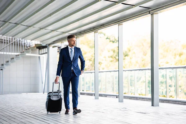 Hombre de negocios guapo y confiado en ropa formal que sostiene la maleta - foto de stock