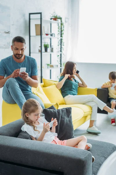 Отец с двумя детьми, использующими смартфоны, пока мама разговаривает по смартфону дома — стоковое фото
