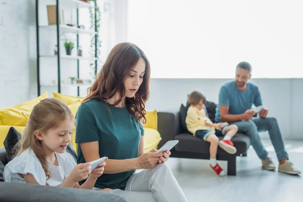 Selektiver Fokus von Mutter und Tochter mit Smartphones in der Nähe von Vater und Sohn mit Smartphones zu Hause — Stockfoto