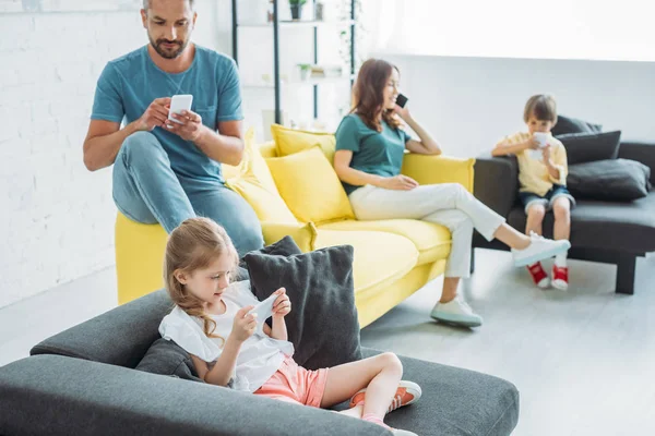 Família sentada em sofás e usando smartphones juntos em casa — Fotografia de Stock