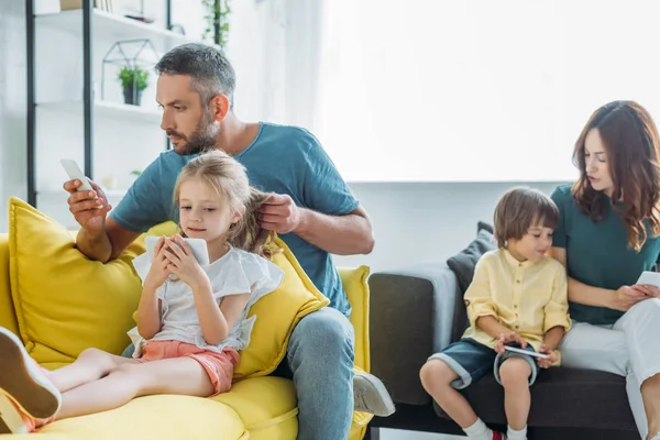 Чоловік і дружина з дочкою і сином сидять на дивані вдома і використовують смартфони — стокове фото