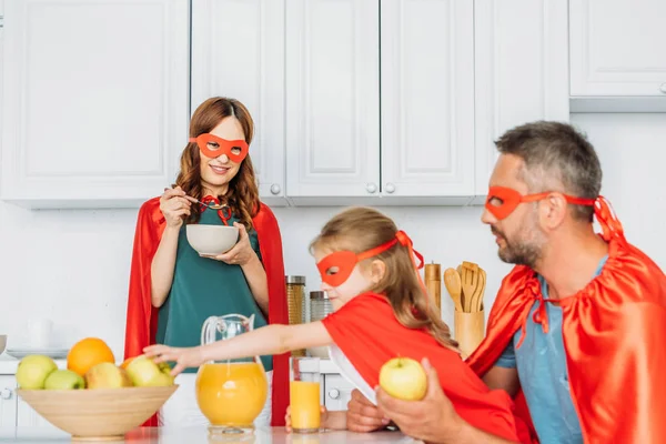 Family in costumes of superheroes having breakfast in kitchen together — Stock Photo