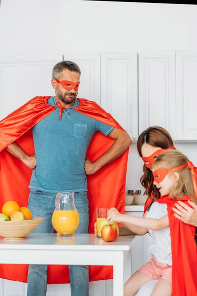 Famiglia in costume di supereroi che fanno colazione, mentre il padre in piedi con le mani sui fianchi — Foto stock