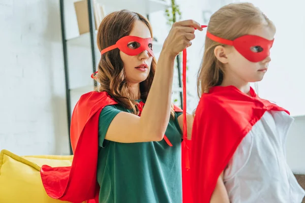 Mulher atenciosa colocando máscara de super-herói na filha bonito — Fotografia de Stock