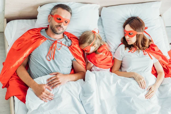 Vista superior de pai, mãe e filha dormindo em trajes de super-heróis — Fotografia de Stock