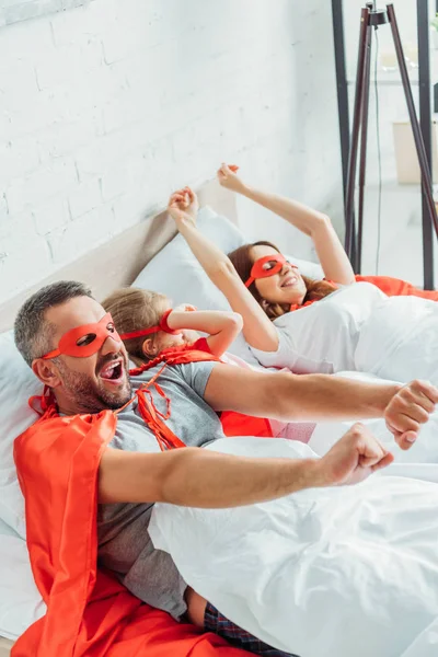 Familia feliz en trajes de superhéroes estirándose mientras se despierta en la mañana - foto de stock