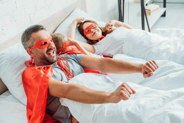 Família feliz em fantasias de super-heróis que se estendem enquanto acordam de manhã — Fotografia de Stock