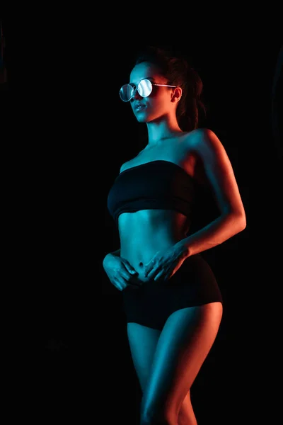 Stylische junge Frau mit Sonnenbrille steht isoliert auf schwarz — Stockfoto