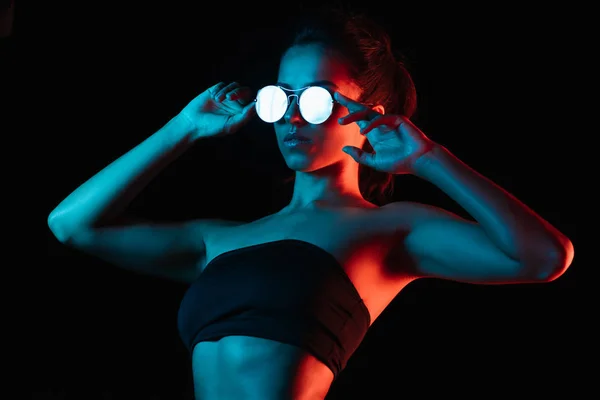 Élégant jeune femme touchant lunettes de soleil isolées sur noir — Photo de stock