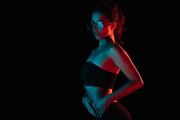 Moda giovane donna in occhiali da sole in piedi con mano in anca isolato su nero — Foto stock