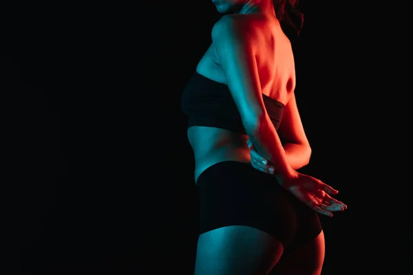 Vista ritagliata di illuminazione su giovane donna in biancheria intima in piedi isolato su nero — Foto stock