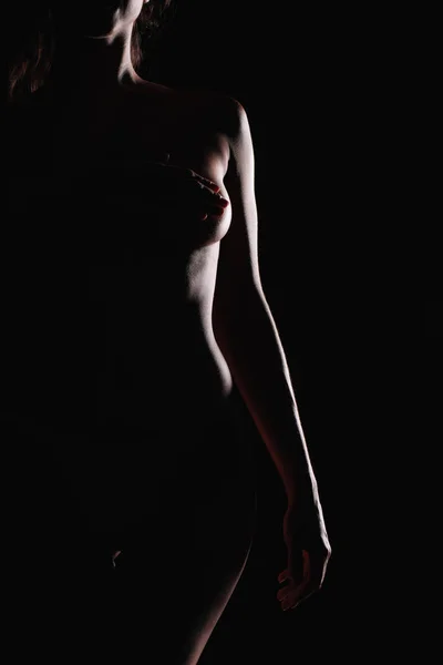 Recortado vista de sexy mujer desnuda de pie y cubriendo los pechos aislados en negro - foto de stock