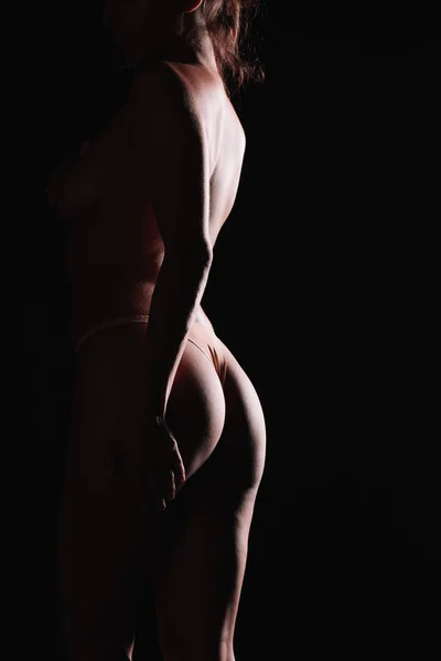 Обрізаний вид роздягненої дівчини, що стоїть в стрингових трусиках ізольовано на чорному — стокове фото