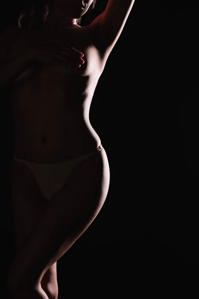Обрізаний вид жінки, що покриває груди рукою, стоячи ізольовано на чорному — стокове фото