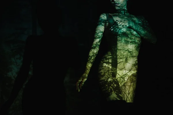 Vista recortada de mujer joven desnuda con sombras en el cuerpo de pie sobre negro - foto de stock