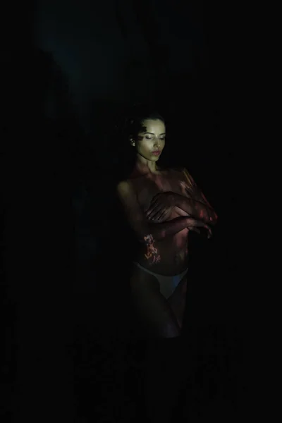 Молода жінка з закритими очима і тінями на тілі, стоячи на чорному — стокове фото