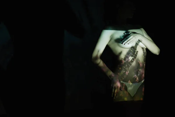 Дівчина покриває груди, стоячи з рукою на стегні на чорному з тінями — стокове фото