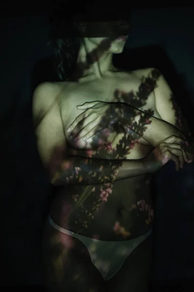 Vue recadrée de la jeune femme couvrant les seins et debout sur noir avec des ombres — Photo de stock