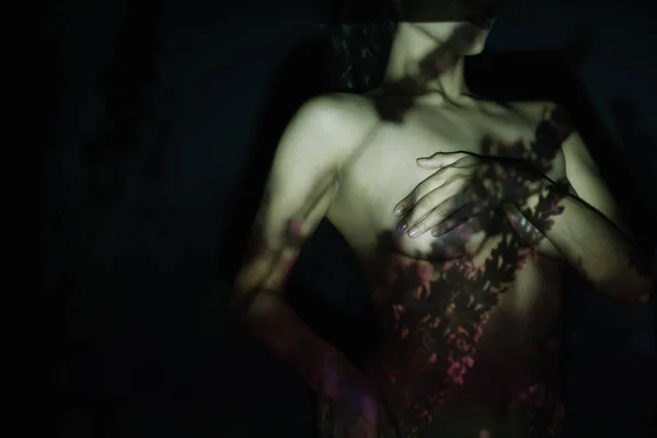 Обрізаний вид роздягненої молодої жінки, що покриває груди, стоячи з рукою на стегні на чорному з тінями — стокове фото