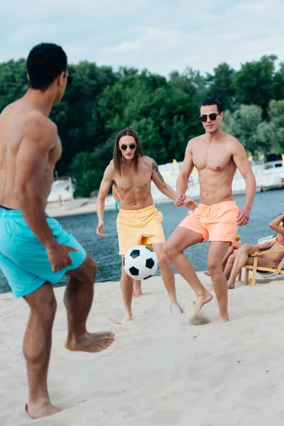 Beaux, jeunes hommes multiculturels jouant au football sur la plage — Photo de stock