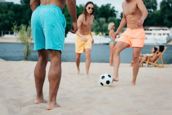 Vista recortada de jóvenes amigos multiculturales jugando al fútbol en la playa - foto de stock