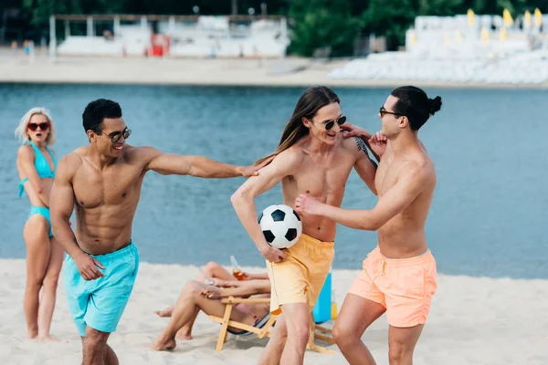 Joyeux, jeunes amis multiculturels s'amuser avec ballon de football sur la plage — Photo de stock