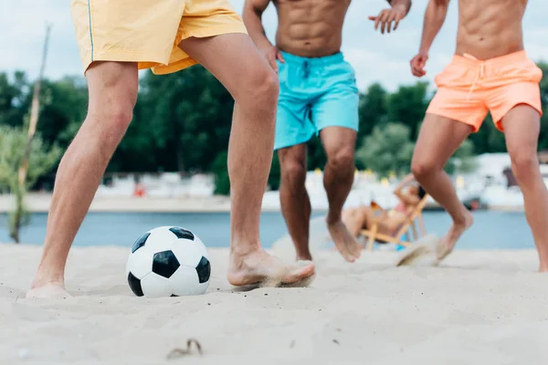 Vue recadrée de jeunes hommes multiculturels jouant au football sur la plage — Photo de stock