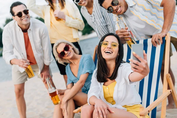 Attractive cheerful woman taking selfie with multicultural friends having fun on beach — Stock Photo