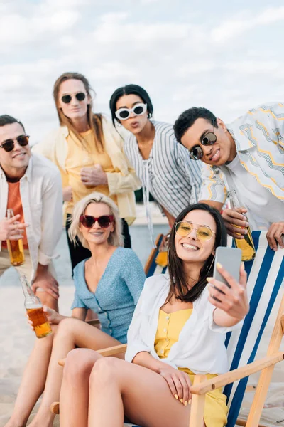 Amigos multiculturales alegres tomar selfie mientras bebe cerveza y divertirse en la playa - foto de stock