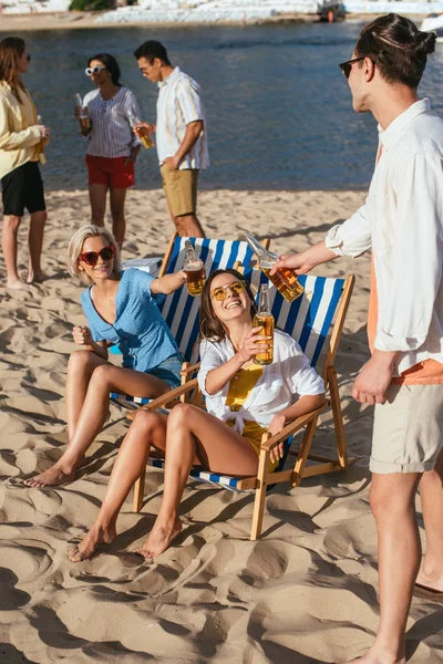 Young multicultural friends smiling and drinking beer while resting on beach — Stock Photo