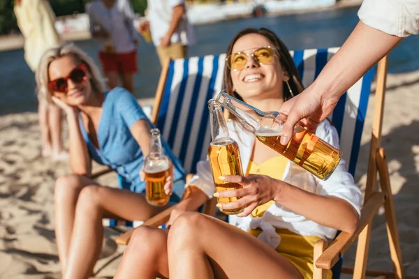 Recortado vista de joven hombre tintineo botellas de cerveza con alegre chica en la playa - foto de stock