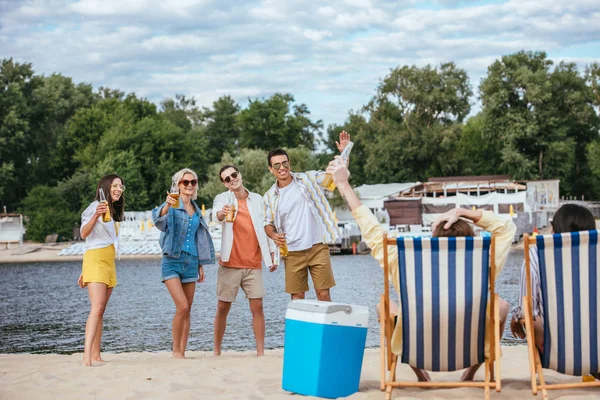 Cheerful multicultural friends holding bottles of beer while resting on beach — Stock Photo