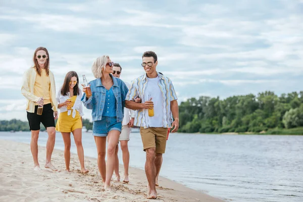 Joven pareja interracial caminando a orillas del río junto con amigos multiétnicos - foto de stock