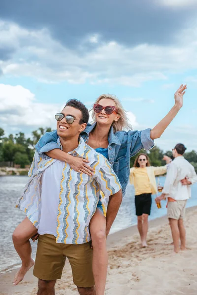 Sourire mixte homme cochonnerie petite amie tout en marchant sur la plage près d'amis multiculturels — Photo de stock