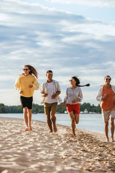 Amici multiculturali felici che corrono sulla spiaggia soleggiata vicino al fiume — Foto stock
