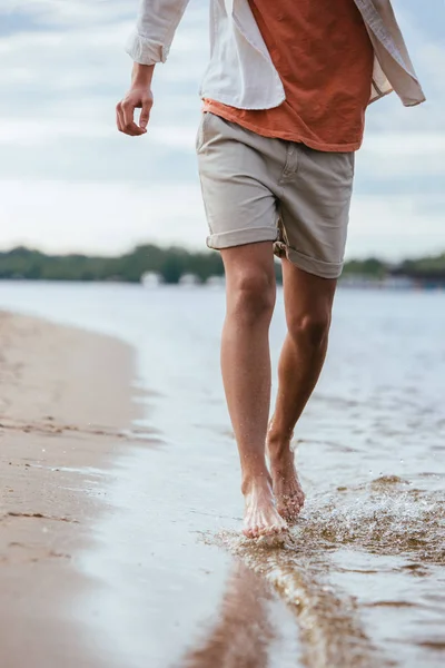 Cropped view of young man in shorts running on riverside — Stock Photo