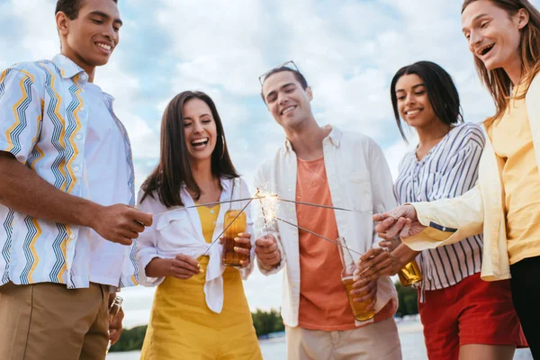 Happy multicultural friends lighting sparklers while having fun on beach — Stock Photo