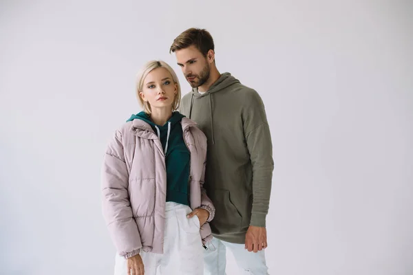 Chica rubia con estilo y hombre barbudo en trajes de otoño aislados en gris - foto de stock