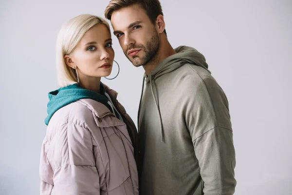 Stylisches blondes Mädchen und bärtiger Mann in herbstlichen Outfits, die vereinzelt in die Kamera auf grau schauen — Stockfoto