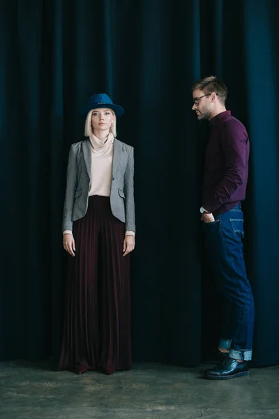 Vista completa de hombre joven con estilo en gafas y mujer rubia en sombrero cerca de la cortina - foto de stock